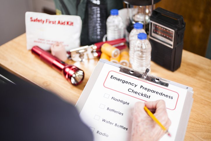 Person checking off emergency checklist with emergency kit items in the background Person checking off emergency checklist with emergency kit items in the background