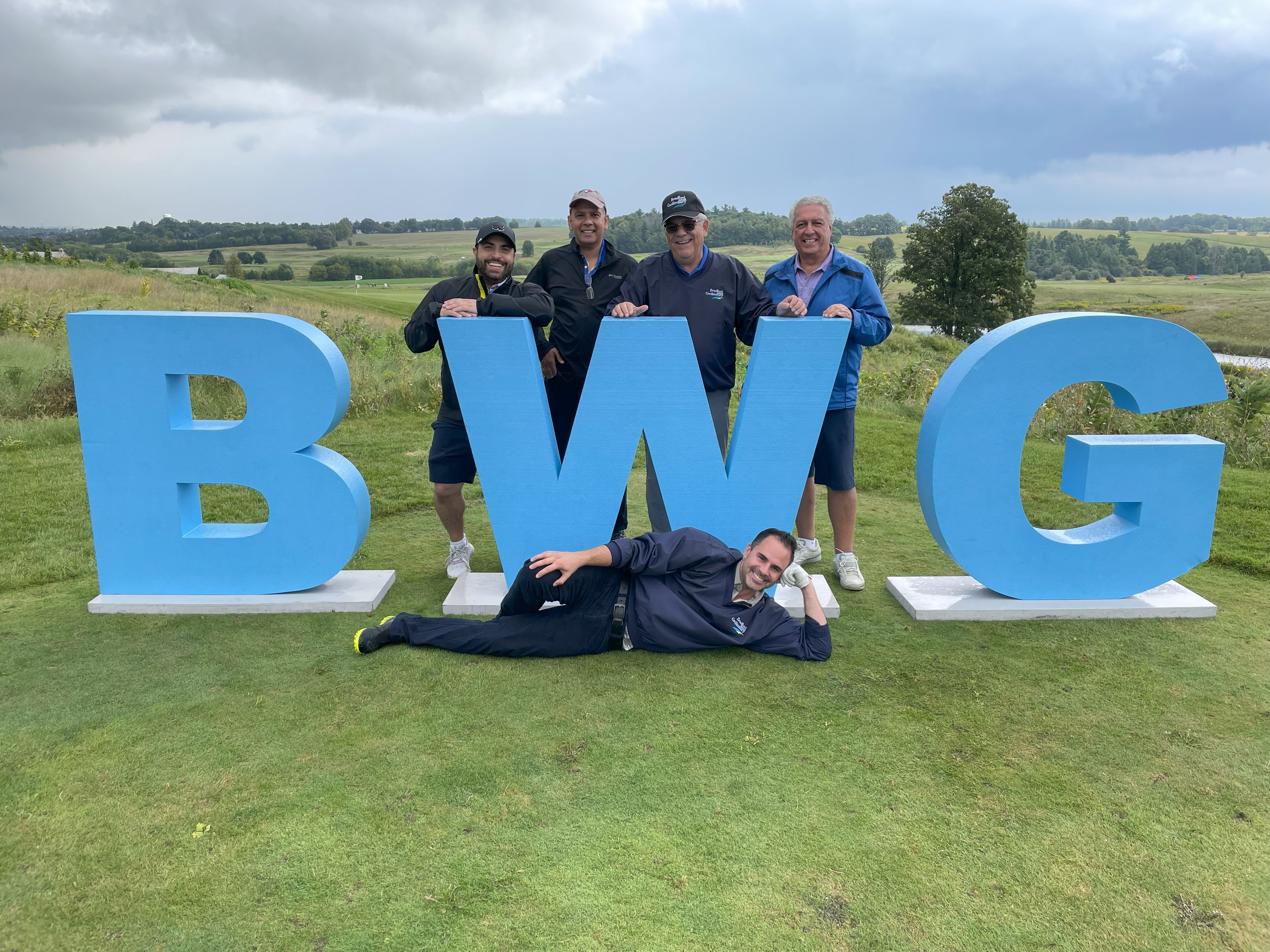 Group of golfers standing on a golf hole behind larger BWG letters. 