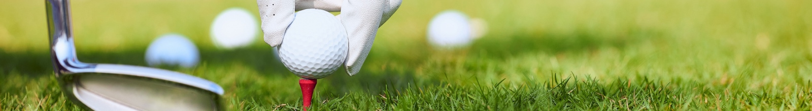 golf ball on a tee with a hand with a golf glove on about to place the ball