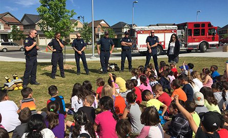 Group of students sitting on a lawn, learning about fire safety from fire prevention staff