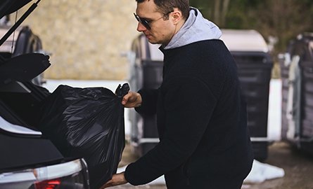 Person taking a garbage back from the back of their vehicle