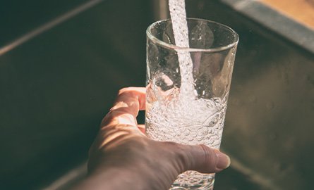 Person pouring tap water in a drinking glass