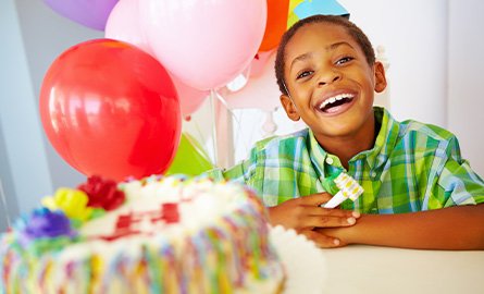 Photo of young boy at his birthday party, colourful balloons in the background