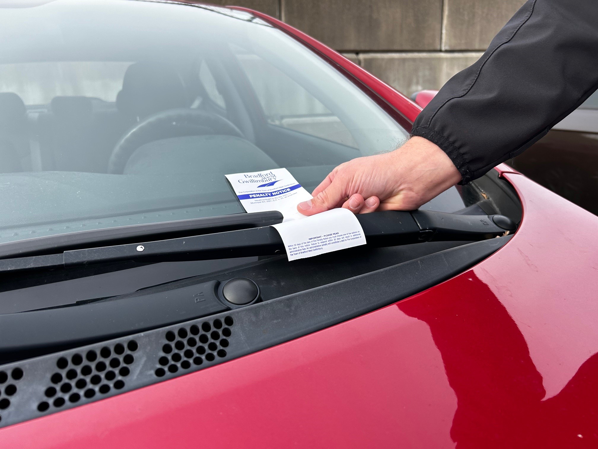 Enforcement officer putting a parking ticket on the front windshield of a red car