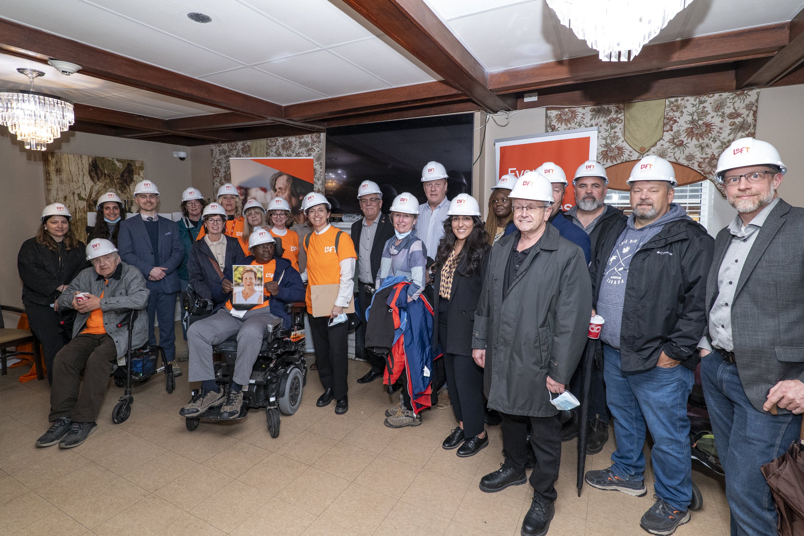 Mayor James Leduc, LOFT Community Service workers, and residents wearing hard hats smiling beside a development sign gathered together outside of the future LOFT Bradford House inside of 31 Frederick Street.