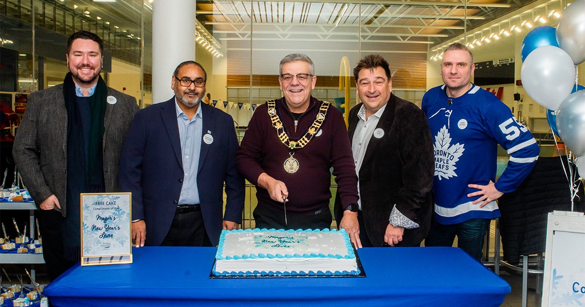 From left to right: Councillor Scott, Deputy Mayor Sandhu, Mayor James Leduc, Councillor Dykie, and Councillor Giordano standing behind a table with a blue tablecloth and cake on top inside of the BWG Leisure Centre 