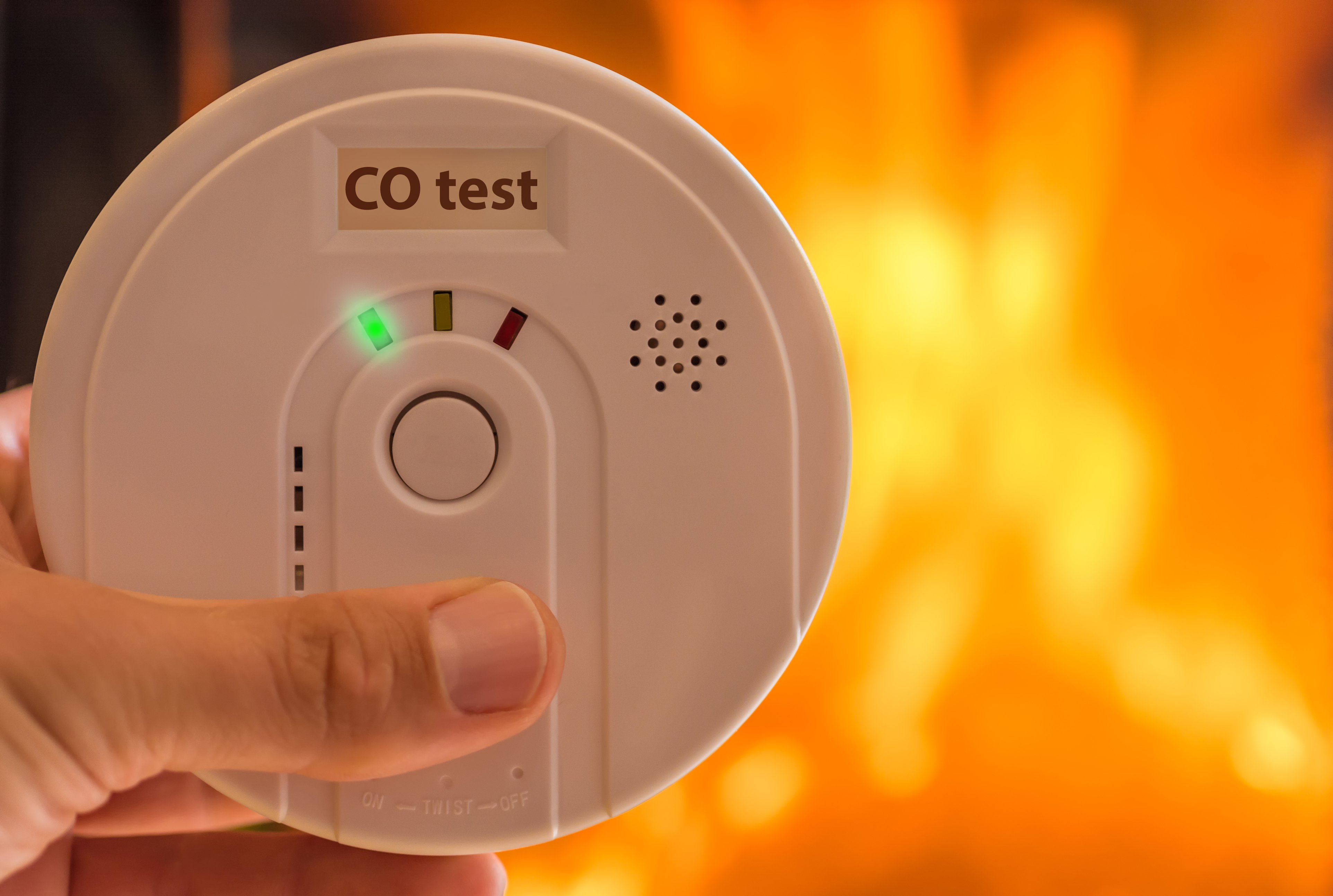 hand on test button of a carbon monoxide detector with flames in background hand on test button of a carbon monoxide detector with flames in background