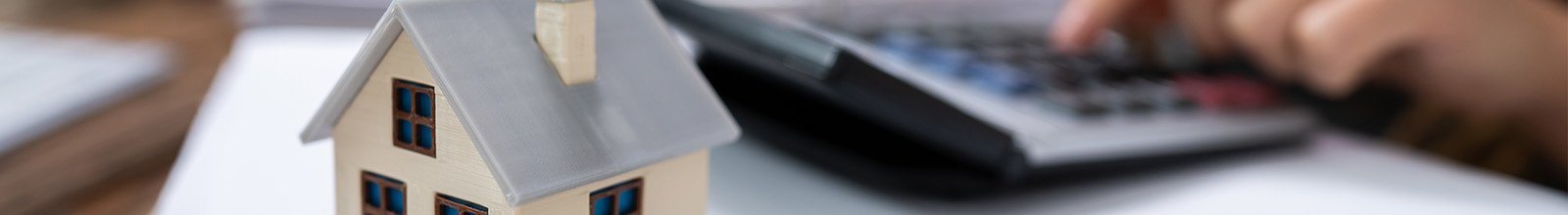 small house on a desk with a calculator and someone using it