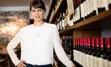 Restaurant business owner standing behind the bar, along a wall lined with wine bottles