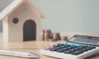 Desk surface with calculator, pen, coins, and a wooden house